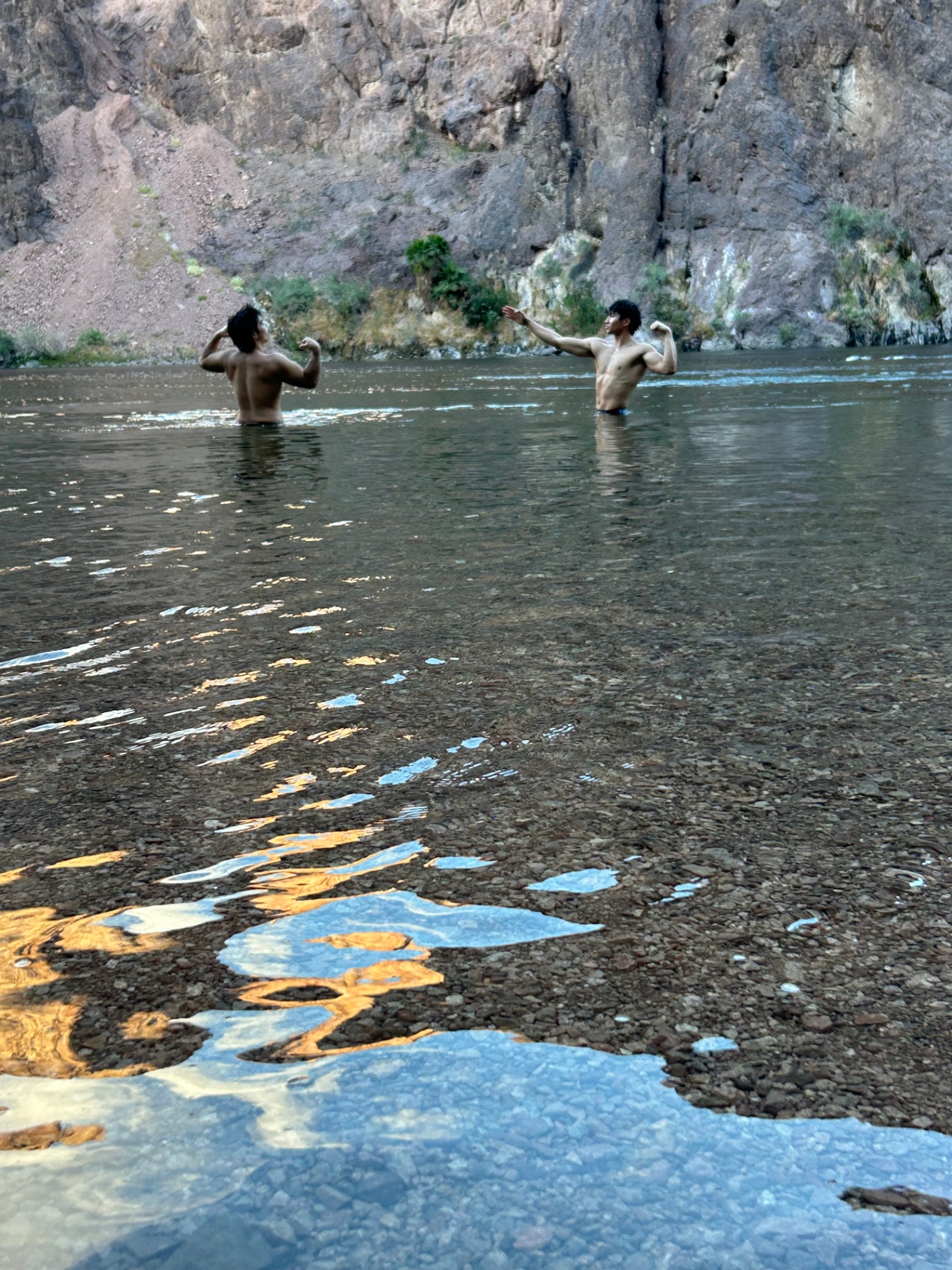 Two athletes posing physiques in a river canyon setting